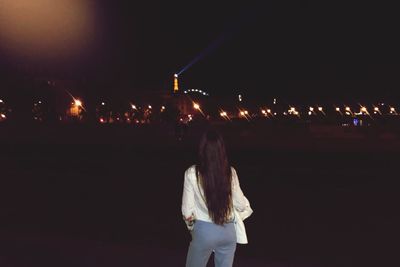 Rear view of people standing on illuminated street at night