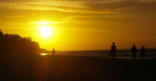 Silhouette people on beach against sky during sunset