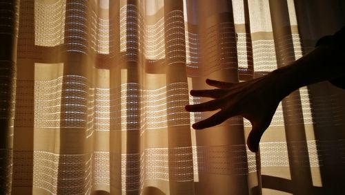 Cropped hand of woman reaching curtain at home