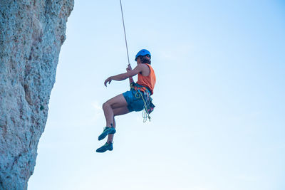 Low angle view of man climbing rope against sky