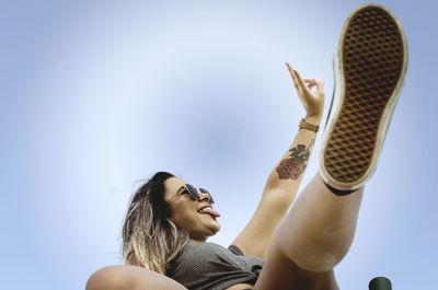 Portrait of a young woman with arms raised against sky