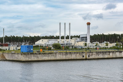 Factory by river against sky