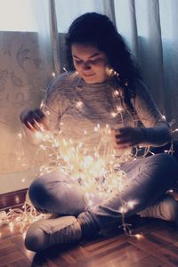 Young woman with illuminated lights sitting at home