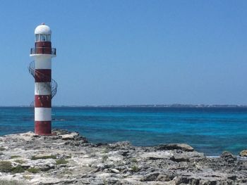 Lighthouse by sea against clear sky