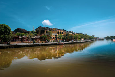 Reflection of houses and trees in lake against blue sky