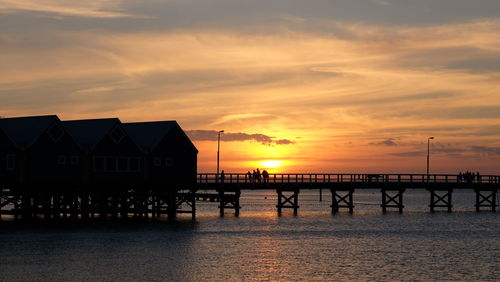 Scenic view of people on jetty against dramatic sky during sunset