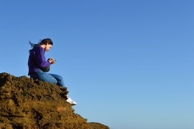 Man sitting on rock against clear blue sky