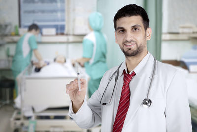 Portrait of smiling doctor holding syringe in hospital