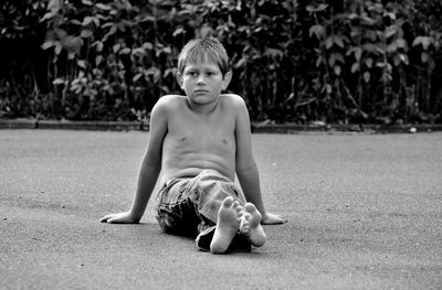 Shirtless boy looking away while sitting on grass against plants