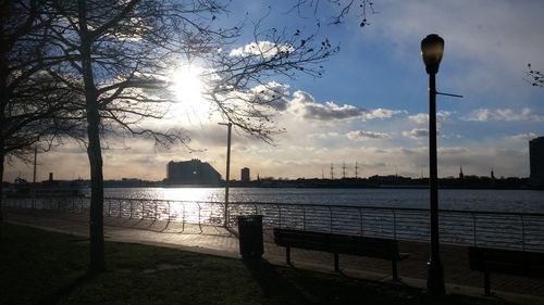 Street light by river against sky during sunset