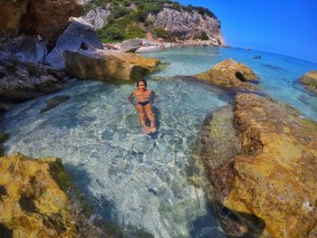 Rear view of shirtless man on rock at sea shore