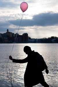 Silhouette man holding balloon by lake