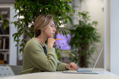 Pensive middle-aged female professor preparing lecture material on laptop in university library