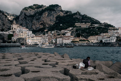 People sitting on rock by sea against sky