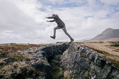 Man jumping on rock against sky