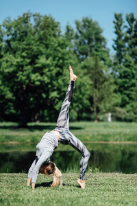 Full length of young woman exercising by pond on field