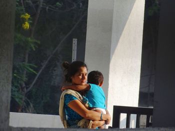 Thoughtful woman carrying child while standing on balcony