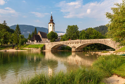 Arch bridge over river by buildings against sky