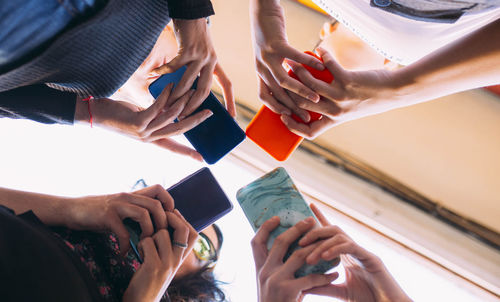 Diverse view from below of young women hands standing together holding smartphones