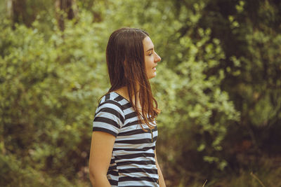 Side view of young woman standing in forest