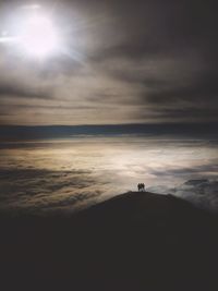 Aerial view of silhouette people standing on mountain against cloudy sky during sunny day