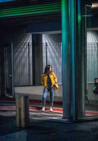 Young woman looking away while standing against building in city at night