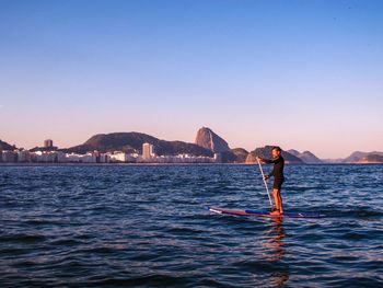 Full length of man paddleboarding in sea against clear sky