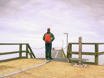 Rear view of man standing on railing against sky