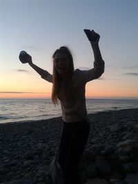 Portrait of excited woman shouting while standing at beach during sunset