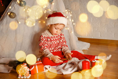 Full length of boy using mobile phone while sitting by christmas decoration