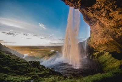 Scenic view of waterfall by cliff against sky