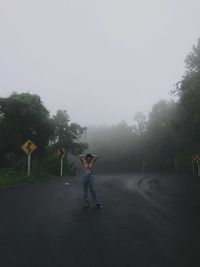 Man standing on road by trees against sky