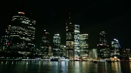 Illuminated city by river against sky at night