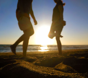 Low section of people on beach against sky during sunset