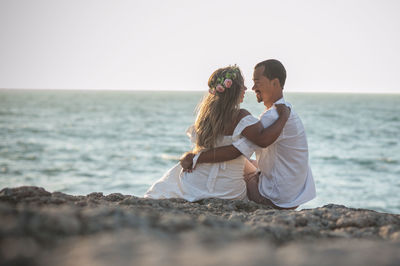 Couple sitting on shore at beach against sky