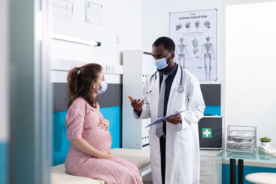 Doctor wearing mask examining pregnant woman in hospital