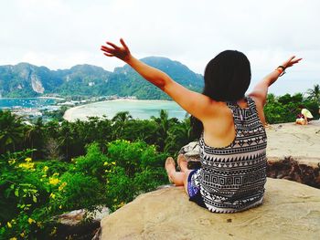 Rear view of woman sitting on rock against sea