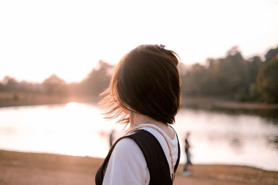 Close-up of woman looking away while standing by lake during sunset