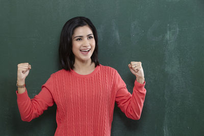 Cheerful female teacher gesturing while standing by blackboard