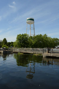 Water tower by lake against sky