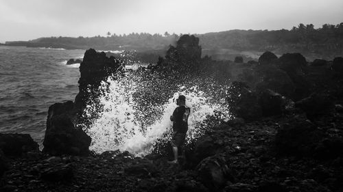 Man standing on rock by sea against sky