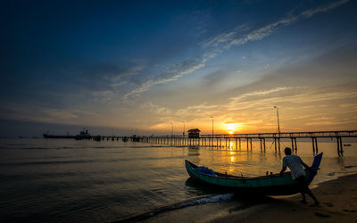 Man pushing boat at beach against sky during sunset