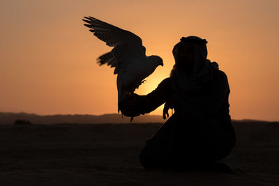 Silhouette man standing at desert against sky during sunset