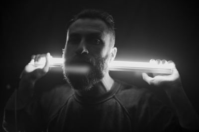 Portrait of young man holding illuminated light against black background