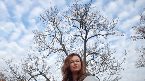 Portrait of young woman against bare tree against sky