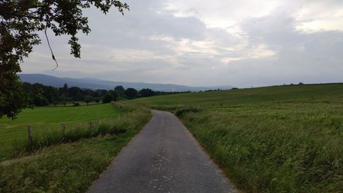 Empty road amidst field against sky