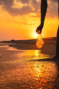 Low section of man walking on beach during sunset