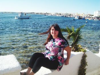 Portrait of smiling young woman sitting on sea against sky