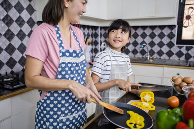 Smiling mother and daughter cooking food in kitchen at home
