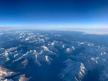 Aerial view of snowcapped mountains against blue sky